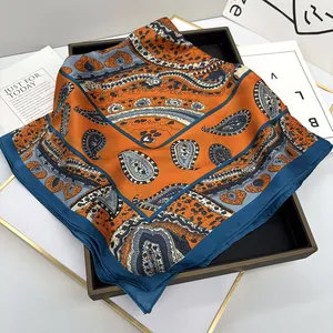 Détail d'un foulard en satin aux motifs paisley orange et bleu sur un plateau noir