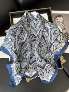 Vista dettagliata di un foulard in seta paisley con bordi blu navy su un vassoio chic