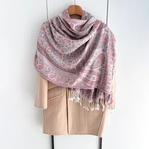 Détail d'un châle à motif cachemire avec franges blanches sur un manteau beige