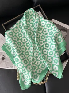 Close-up of square satin scarf with green checkered daisy floral pattern and silk texture