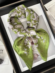 Détail d'un foulard en soie vert à motif cachemire avec bords roulés sur un magazine chic