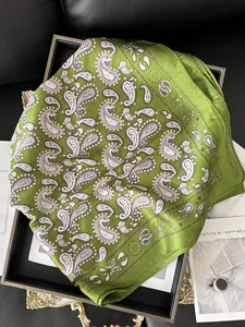 Détail du foulard en soie verte à motif cachemire sur un plateau de présentation