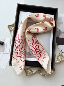 Détail d'un foulard en soie champagne avec motifs paisley rouges posé sur un plateau chic