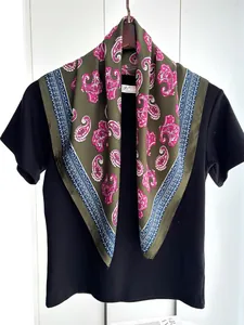 Detailed view of paisley pattern scarf in olive green and pink on a black display stand