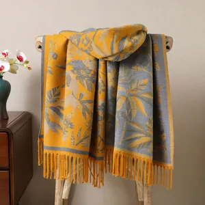 Détail d'une écharpe jaune gingembre et grise avec motif jacquard floral et franges