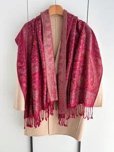 Détail d'un châle jacquard rouge à motif paisley avec franges sur manteau beige
