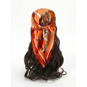 Elegant orange silk square scarf with vintage belt print worn as a stylish headband
