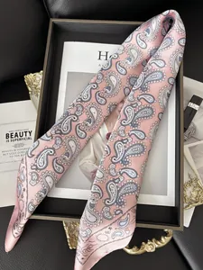 Détail d'un foulard en soie rose à motif paisley sur un plateau de luxe avec magazine