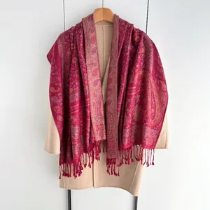 Châle cachemire rouge foncé à motifs paisley et franges sur un manteau beige élégant