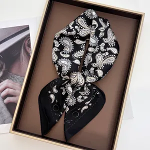 Détails d'un foulard carré en soie présentant des motifs paisley noirs et dorés