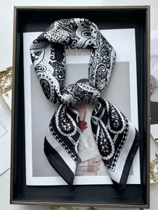 Close-up of a black and white paisley silk scarf in a stylish gift box on marble