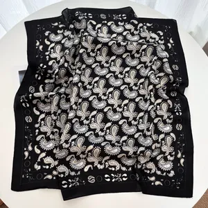 Détail du foulard en soie montrant le motif cachemire blanc sur tissu satiné noir