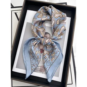 Carré de soie bleu clair à motif paisley pour femme présenté dans un plateau élégant