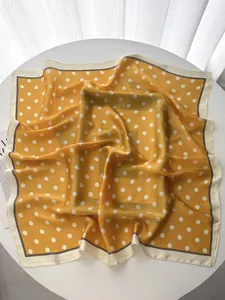Detail of yellow polka dot silk scarf draped on a white table in elegant soft light