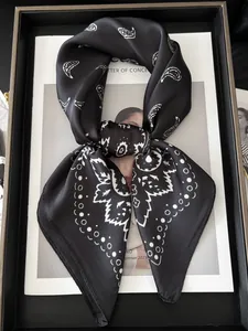 Détail d'un foulard en soie synthétique avec motif paisley blanc sur satin noir lisse