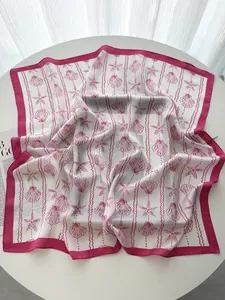 Detailed flat lay of silk square scarf with pink seashell and starfish prints on a white table