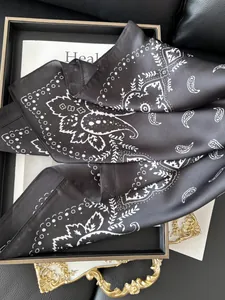 Détail d'un foulard en soie noir avec motif cachemire blanc sur un plateau doré