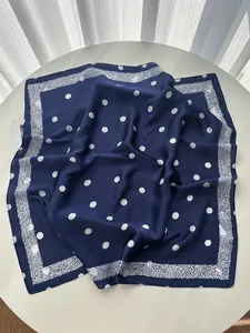 Detailed view of dark blue silk scarf with white polka dots and elegant patterned border