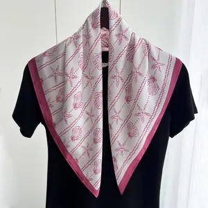 Detail of a square silk scarf with pink starfish and seashell prints on a black t-shirt