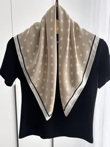 Detail of champagne silk scarf with white polka dots and high-contrast black and white border