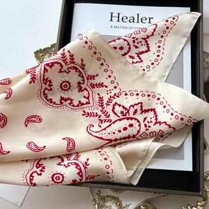 Carré de soie crème élégant avec motifs paisley rouges présenté sur un plateau de luxe