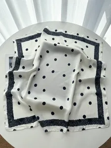 Detailed view of elegant ivory silk scarf with large black polka dots and textured border