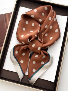 Detailed close-up of brown polka dot silk scarf with smooth satin texture in a gift box