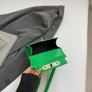 Bright green crocodile pattern mini crossbody bag with metal twist lock on a desk
