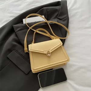Minimalist beige leather handbag with gold U-ring buckle and crossbody strap beside a phone