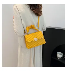 Detailed view of yellow quilted handbag with heart buckle and pleated handle