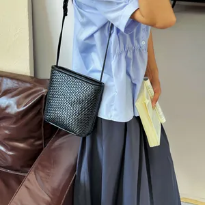 Sac seau tissé noir minimaliste pour femme porté en bandoulière sur un mannequin