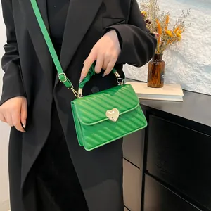Green pleated handbag with gold heart buckle shown in a lifestyle fashion setting