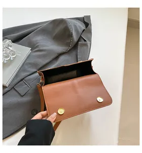 Detail van bruine PU-leren crossbodytas met dubbele magnetische gouden gespen op de klep