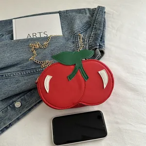 Fashionable red cherry shaped shoulder bag with gold chain strap on blue denim background