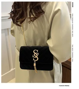 Detail of black velvet quilted chain bag with gold metal logo and tassel on trench coat