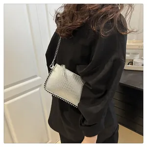 Silver crocodile texture crossbody bag with metal chain strap and rivet details on the edge