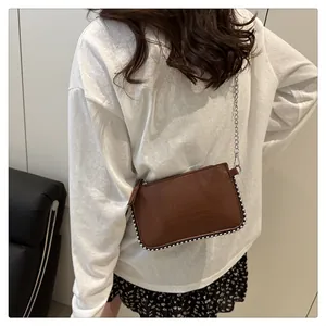 Close-up of brown faux-crocodile texture handbag with silver bead trim and chain
