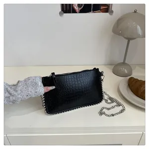 Macro detail of black crocodile texture bag with silver metal studs and chain strap