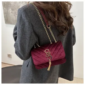 Detailed texture of burgundy velvet crossbody bag with chevron quilting and golden tassel