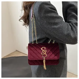 Detail of burgundy velvet crossbody bag with V-quilted stitching and gold tassel hardware