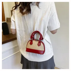 Detail of woven straw shell bag with red leather trim and metal chain strap on model