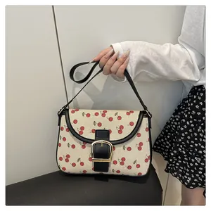 Close-up of cherry print canvas bag with black leather trim and golden metal buckle