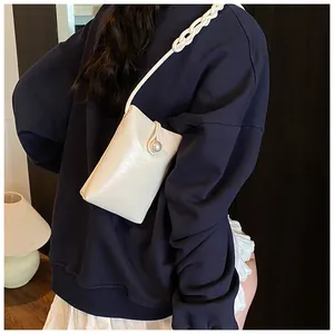 Detail showing creamy white crossbody phone bag with large pearl buckle and woven strap