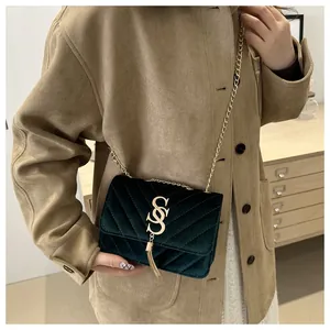 Detail of dark green velvet quilted bag with gold S logo, tassel, and chain strap