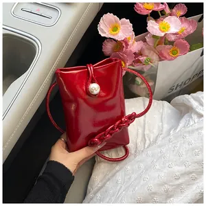 Macro view of a mini red patent leather crossbody bag with a large pearl buckle detail
