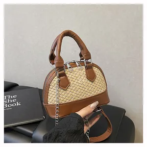 Detail of woven and brown faux leather shell bag with metal chain strap held by hand