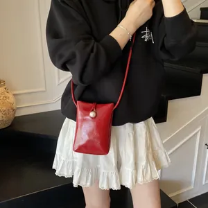 Mini red glossy crossbody bag with pearl closure worn over a black sweatshirt
