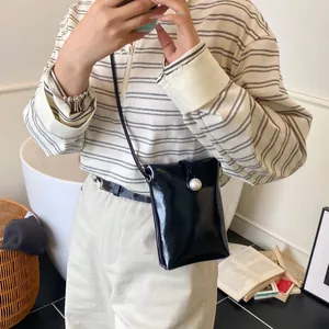 Mini black patent leather crossbody bag with a large pearl buckle and slim shoulder strap