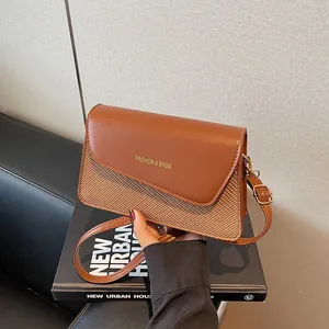 Braune Umhängetasche aus Leder und Gewebe mit goldenem Schriftzug auf dem Sofa