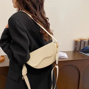 Sacoche selle beige avec bandoulière large et boucles dorées sur blazer noir chic